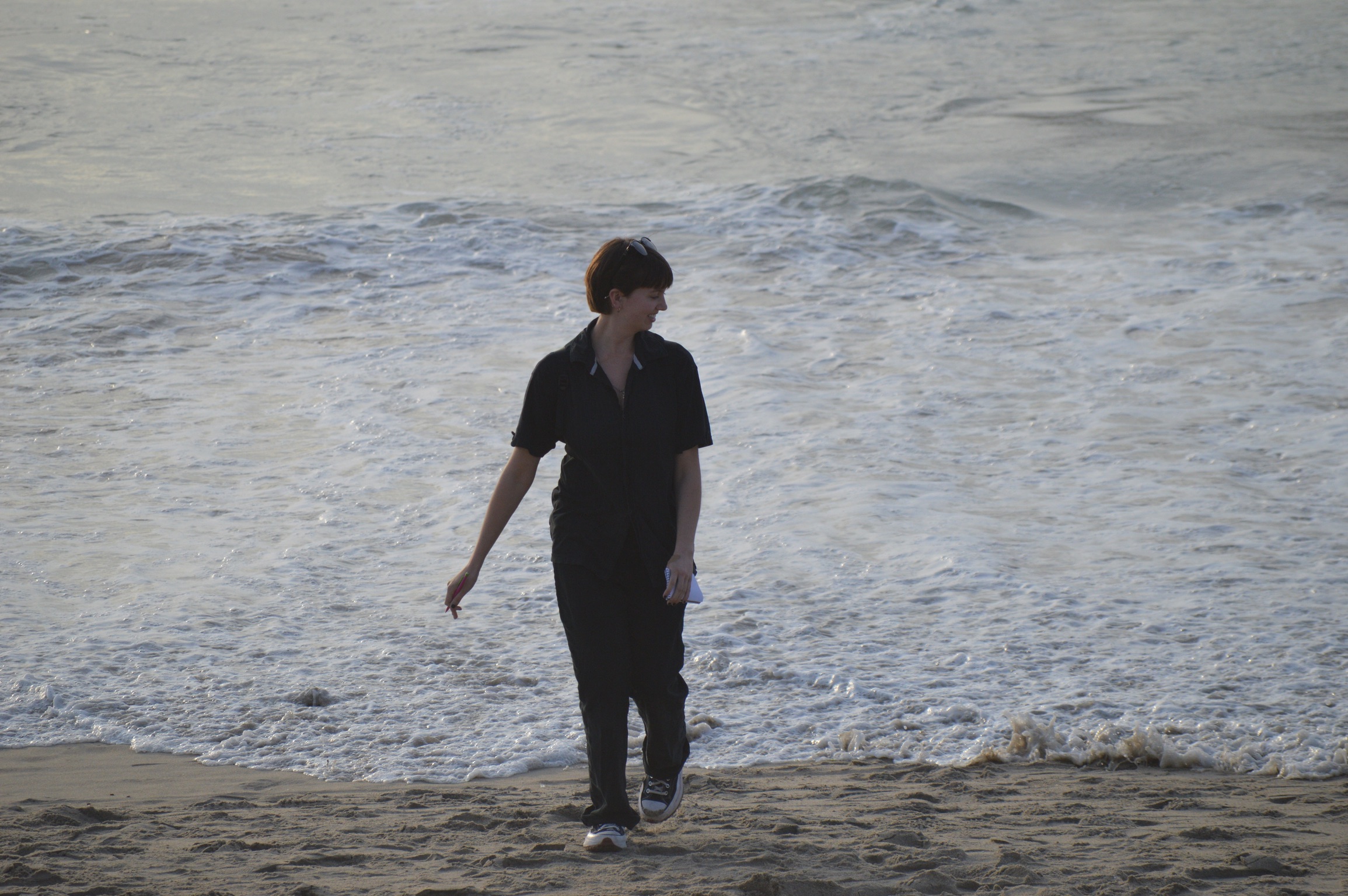 Caroline King walking on a beach with a pen and notebook in hand.